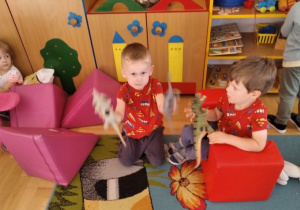 Chłopcy bawią się dinozaurami, w tle siedzi dziewczynka.